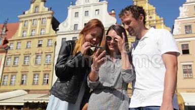 在阳光明媚的夏<strong>日</strong>里，三个朋友在旧<strong>建筑</strong>背景下使用<strong>手机</strong>的户外肖像。